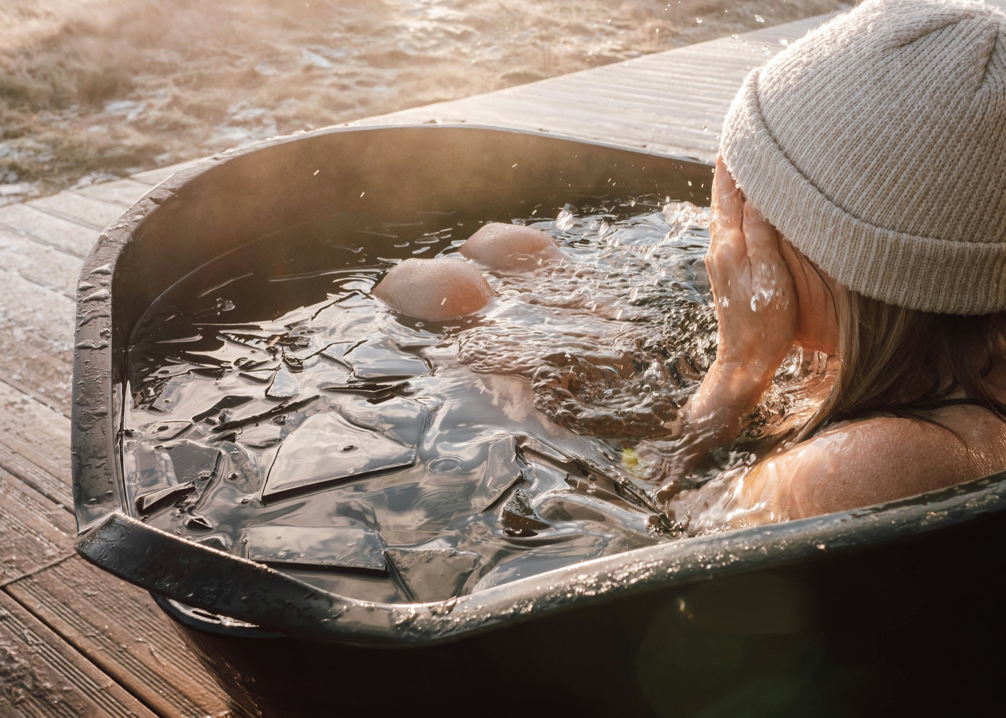 Hands covering a face in an ice bath, backlit in gold