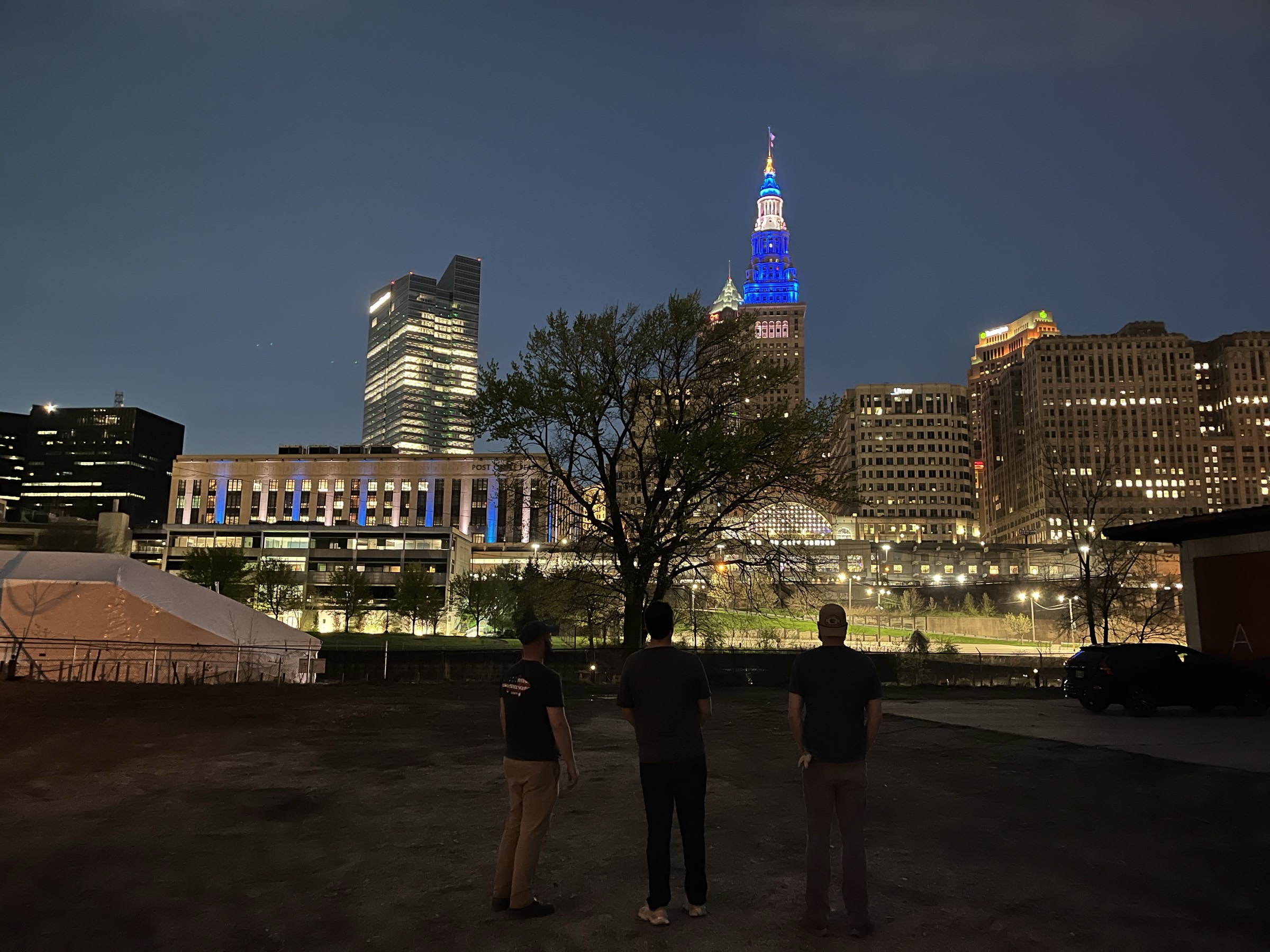 The three Saunagoose founders standing on the lot, facing the Cleveland skyline at night