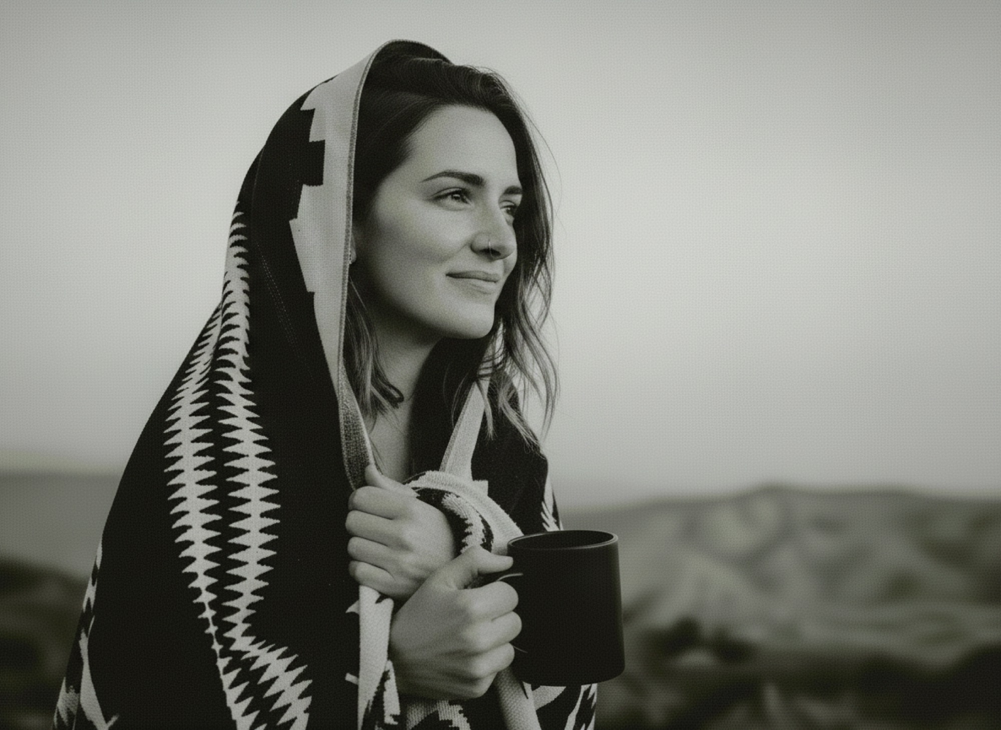 A woman wrapped in a patterned blanket, holding a dark mug